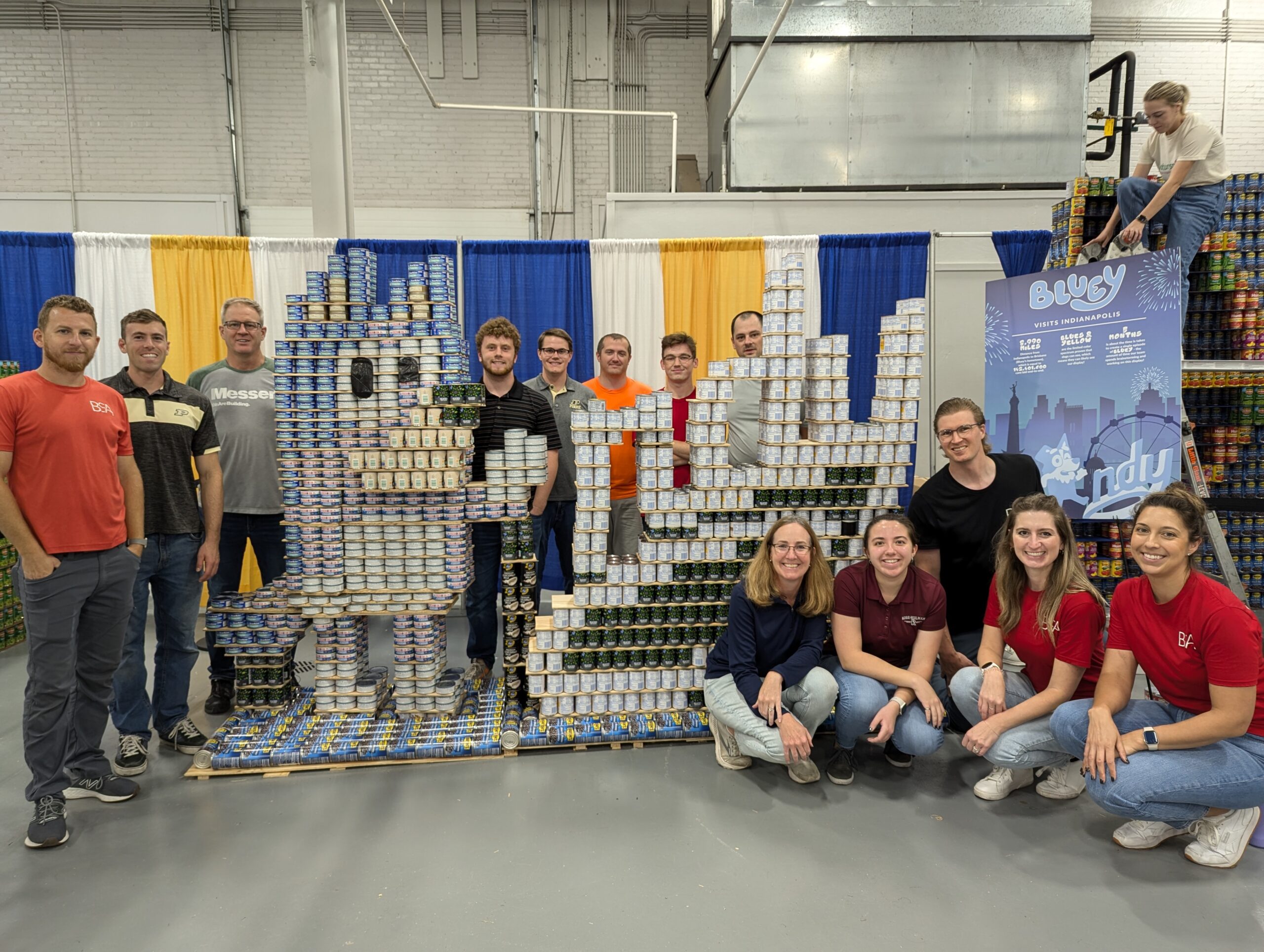 Messer Construction employees in Indianapolis standing in front of canned goods stacked and shaped as the Bluey cartoon